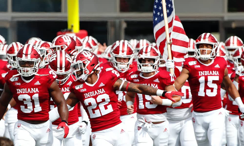 Indiana Hoosiers football players running onto the field while holding an American flag